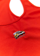 A red Audi crop top for women. Photo is a close up view of the top with an embroidered Audi Sport Quattro S1 E2. Fabric composition is polyester, and cotton. The material is stretchy, ribbed, and non-transparent. The style of this shirt is sleeveless, with a scoop neckline.