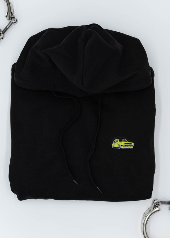 A black VW Volkswagen unisex hoodie for men and women. Photo is a front view of the sweater with an embroidered modified green Mk1 Golf. Fabric composition is cotton, polyester, and rayon. The material is very soft, stretchy, and non-transparent. The style of this hoodie is long sleeve, crewneck with a hood, hooded, with embroidery on the left chest.