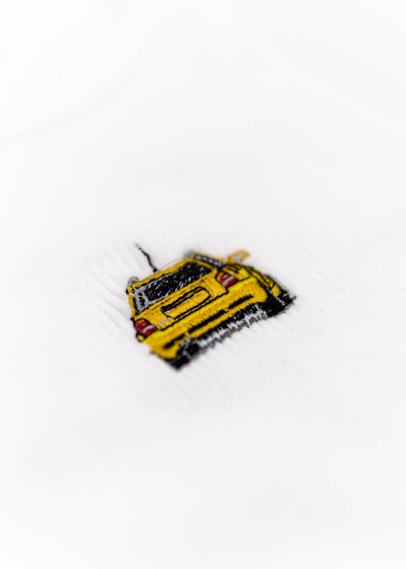 A white Audi crop top for women. Photo is a close up view of the top with an embroidered Imola Yellow Audi B5 RS4. Fabric composition is polyester, and elastine. The material is stretchy, ribbed, and non-transparent. The style of this shirt is sleeveless, with a crewneck neckline.