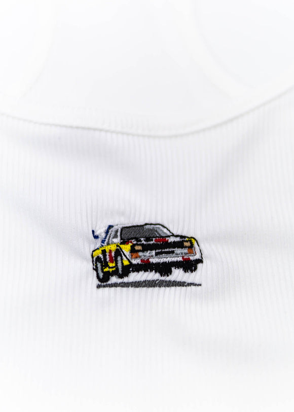 A white Audi crop top for women. Photo is a close up view of the top with an embroidered Audi Sport Quattro S1 E2. Fabric composition is polyester, and cotton. The material is stretchy, ribbed, and non-transparent. The style of this shirt is sleeveless, with a scoop neckline.
