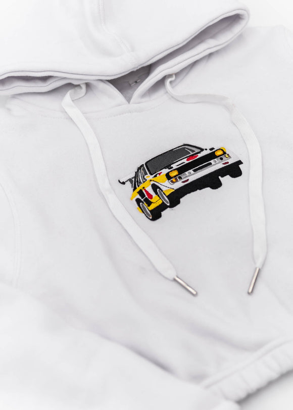 A white Audi cropped hoodie for women. Photo is a front view of the cropped sweater with an embroidered Sport Quattro S1 E2. Fabric composition is cotton, and polyester. The material is soft, stretchy, and non-transparent. The style of this crop hoodie is long sleeve, crewneck with a hood, hooded, with embroidery on the chest.