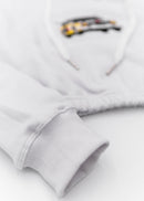 A white Audi cropped hoodie for women. Photo is a front view of the cropped sweater with an embroidered Sport Quattro S1 E2. Fabric composition is cotton, and polyester. The material is soft, stretchy, and non-transparent. The style of this crop hoodie is long sleeve, crewneck with a hood, hooded, with embroidery on the chest.