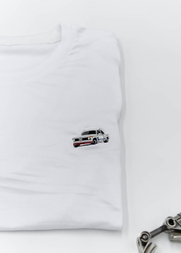A white BMW 2002 Turbo t-shirt for men. Photo is a close up of the shirt with an embroidered 2002 Turbo. Fabric composition is a polyester and cotton mix. The material is very soft, stretchy, non-transparent. The style of this shirt is short sleeve, with a crewneck neckline.