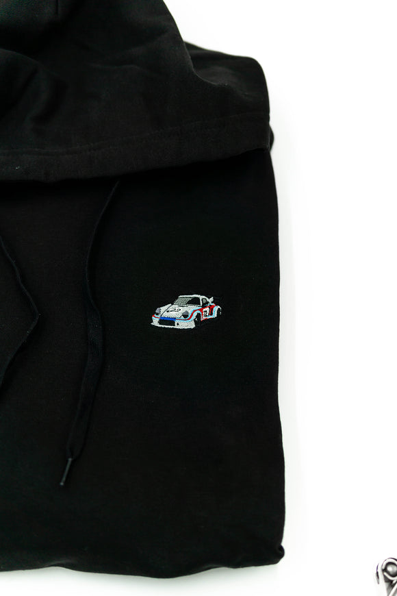 A black 911 RSR racing unisex hoodie for men and women. Photo is a close up view of the sweater with an embroidered Martini R13 911 RSR 2.1 Turbo. Fabric composition is cotton, polyester, and rayon. The material is very soft, stretchy, and non-transparent. The style of this hoodie is long sleeve, crewneck with a hood, hooded, with embroidery on the left chest.