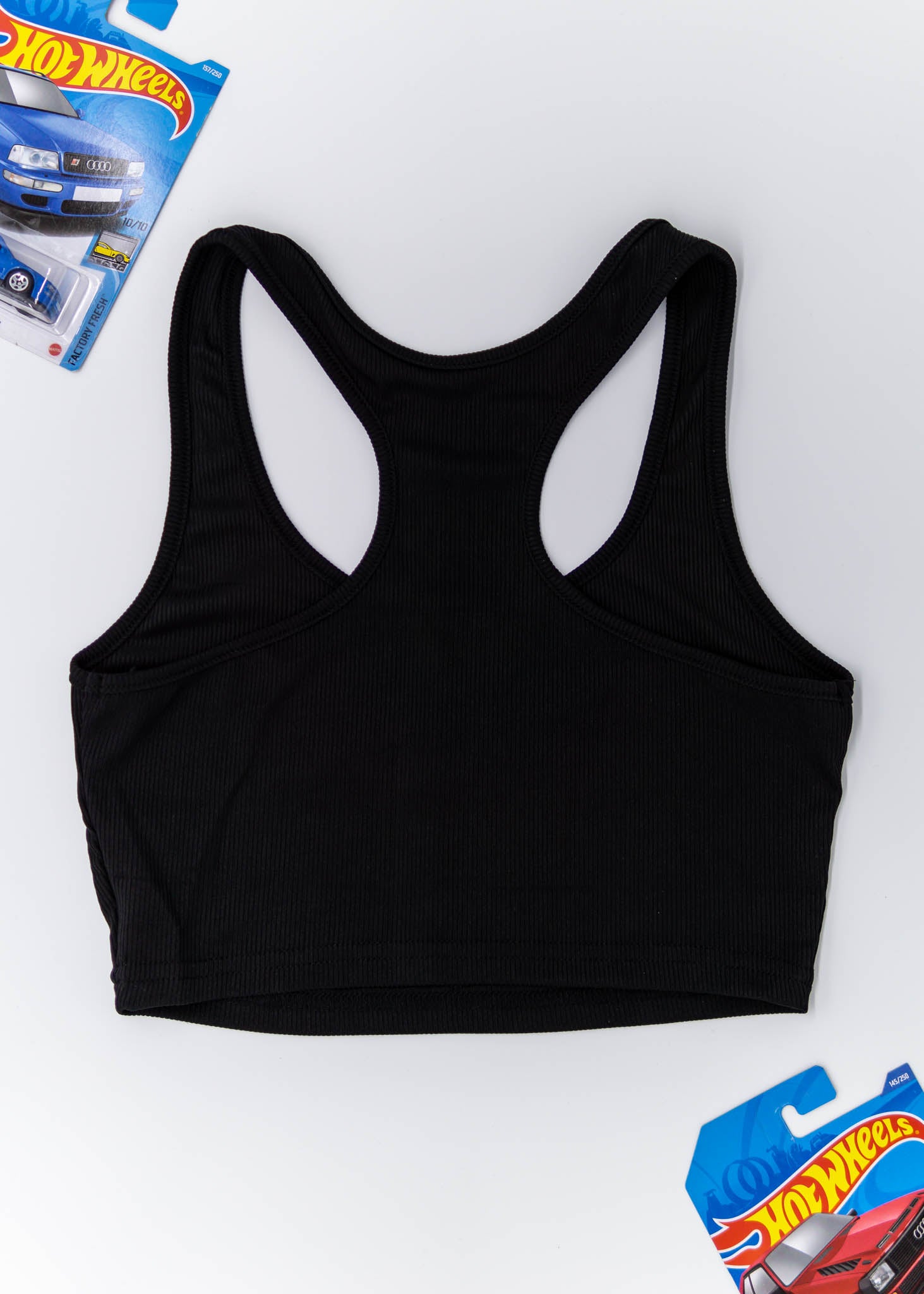 A black Audi crop top for women. Photo is a blank canvas back view of the top with an embroidered imola yellow Audi B5 RS4. Fabric composition is polyester, and elastine. The material is stretchy, ribbed, and non-transparent. The style of this shirt is sleeveless, with a crewneck neckline.