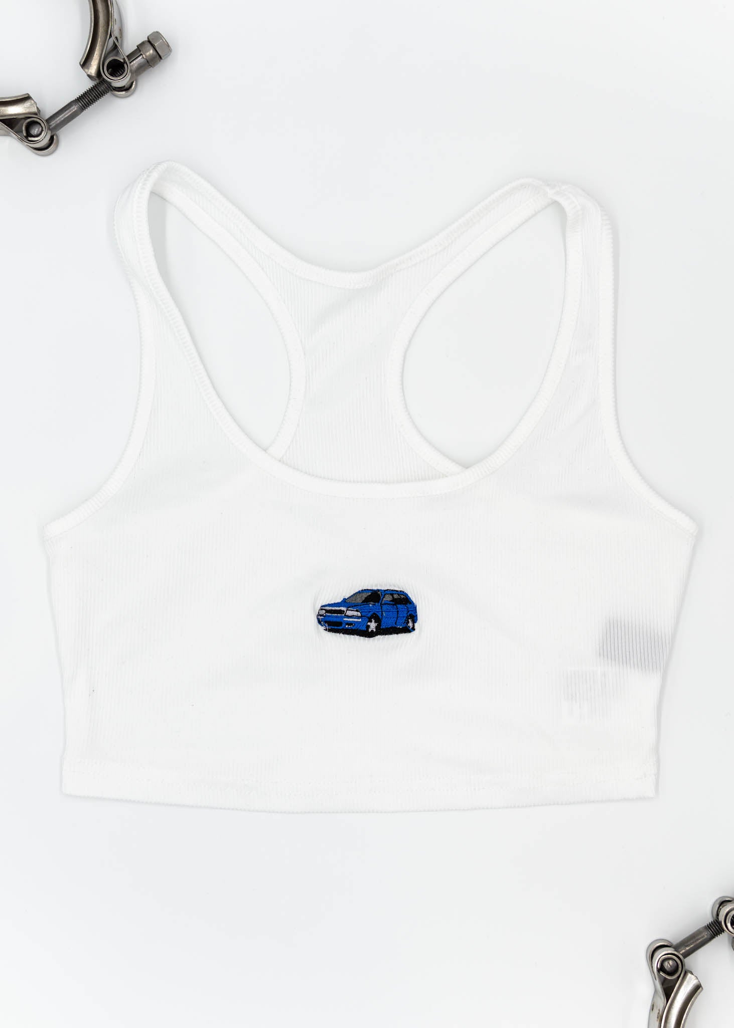 A white Audi crop top for women. Photo is a front view of the top with an embroidered Nogaro Blue Audi 80 RS2 Avant made by Porsche. Fabric composition is polyester, and cotton. The material is stretchy, ribbed, and non-transparent. The style of this shirt is sleeveless, with a scoop neckline.