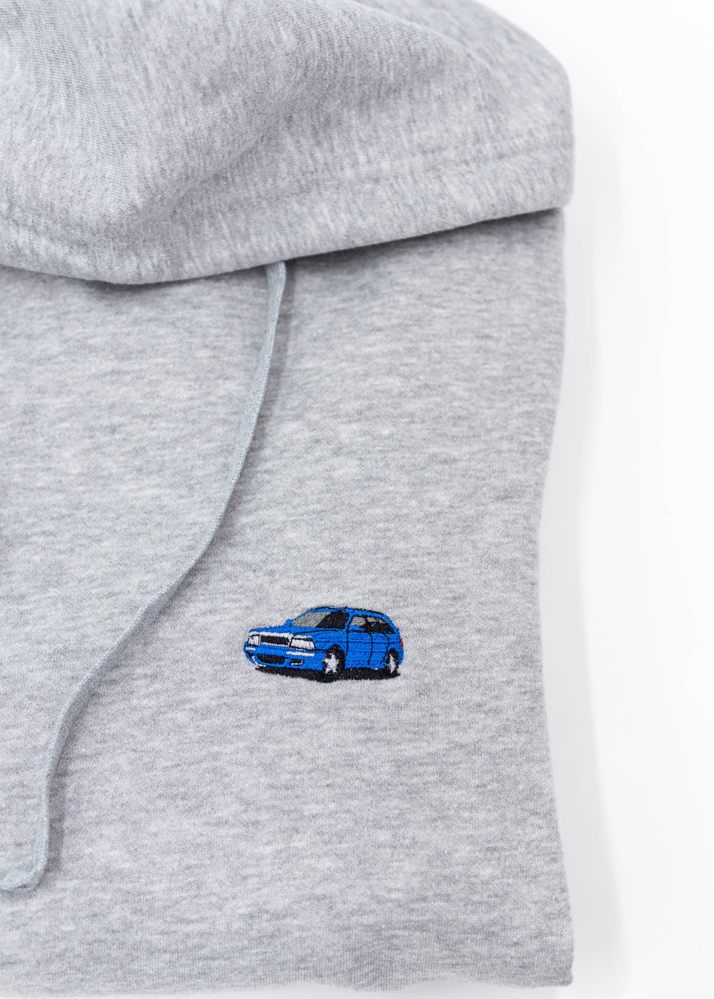 A grey Audi unisex hoodie for men and women. Photo is a close up view of the sweater with an embroidered Nogaro Blue Audi 80 RS2 Avant made by Porsche. Fabric composition is cotton, polyester, and rayon. The material is very soft, stretchy, and non-transparent. The style of this hoodie is long sleeve, crewneck with a hood, hooded, with embroidery on the left chest.