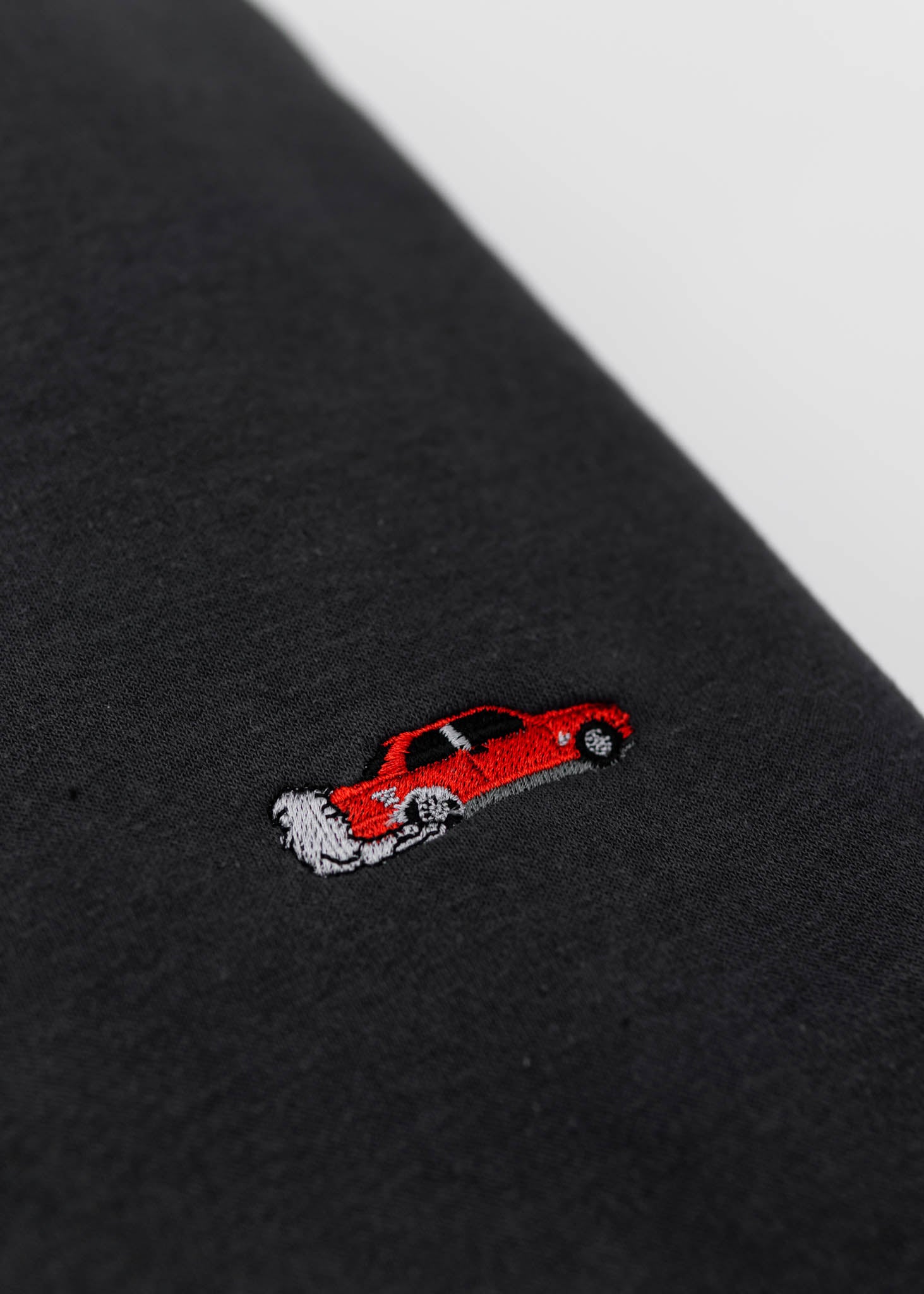 A dark grey BMW/Bimmer E30 M3 crewneck sweater for men. Photo is a close up of the sweater with an embroidered red BMW E30 M3 doing a burnout. Fabric is 100% cotton and high quality and fits to size. The style is long sleeve, crew neck, and embroidery on left chest.