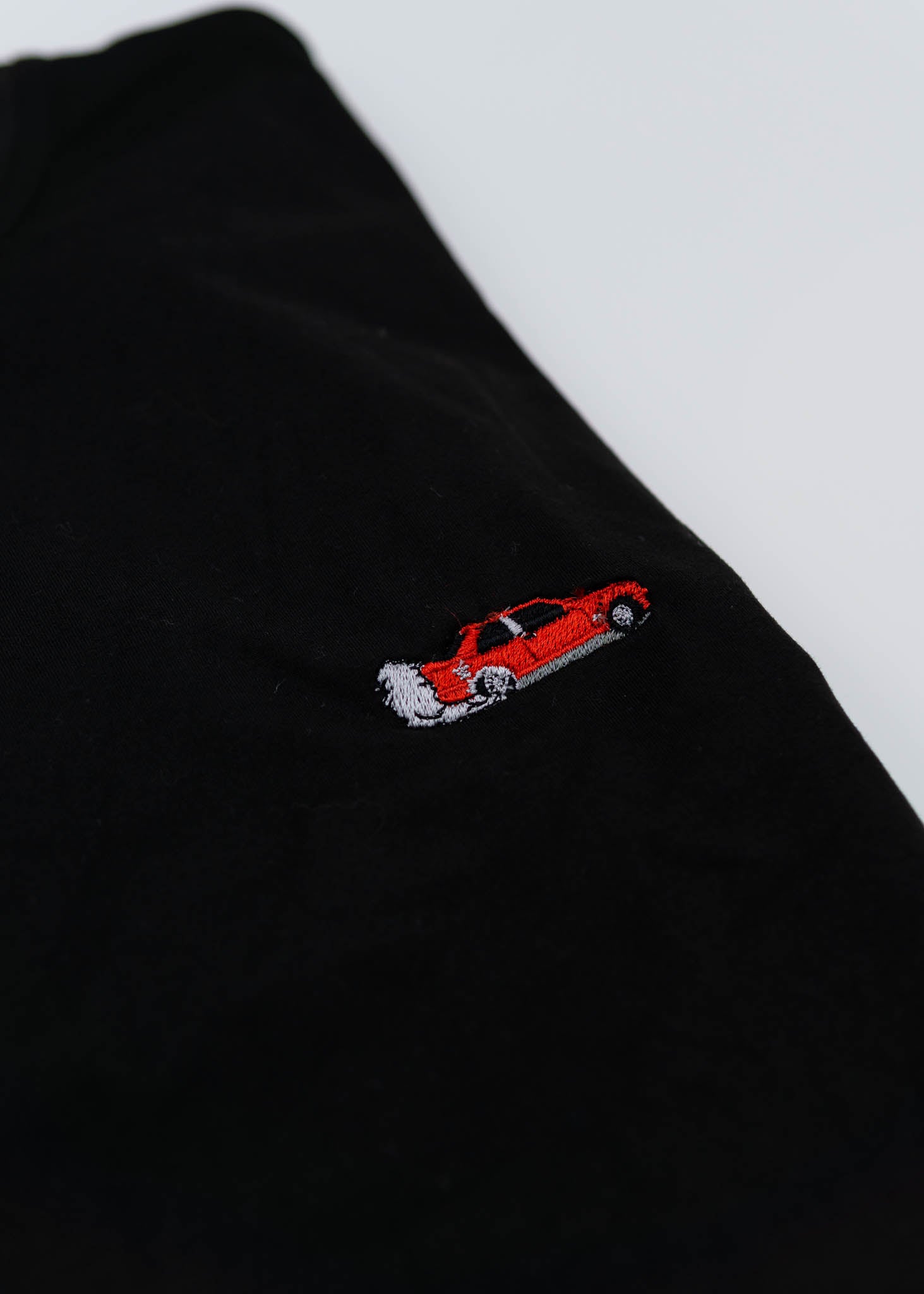 A black BMW/Bimmer E30 M3 T-Shirt for men. Photo is a close up of the shirt with an embroidered Red BMW E30 M3 Coupe. Fabric composition is 100% polyester. The material is very stretchy, soft, comfortable, breathable, and non-transparent. The style of this shirt is short sleeve, with a crewneck neckline.
