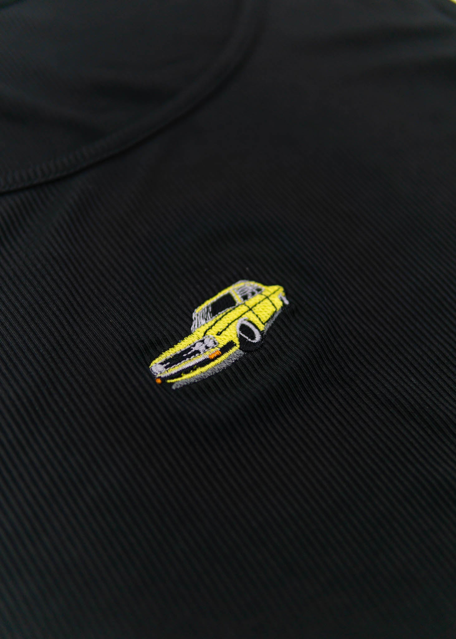 A black Audi crop top for plus sized women. Photo is a close up front view of the top with an embroidered yellow Audi 100LS. Fabric composition is polyester, and elastine. The material is stretchy, ribbed, and non-transparent. The style of this shirt is sleeveless, with a round neckline.