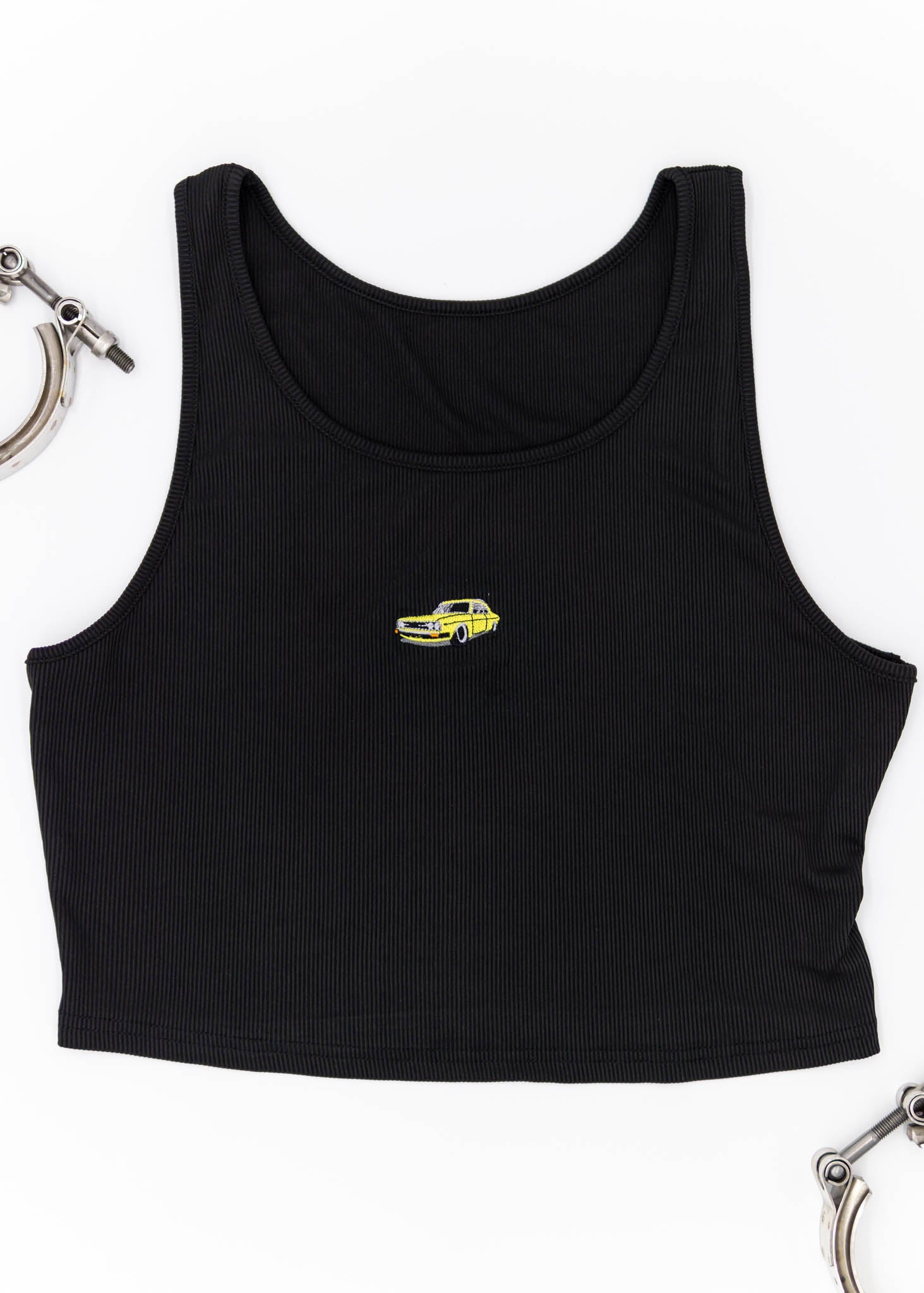 A black Audi crop top for plus sized women. Photo is the front view of the top with an embroidered yellow Audi 100LS. Fabric composition is polyester, and elastine. The material is stretchy, ribbed, and non-transparent. The style of this shirt is sleeveless, with a round neckline.