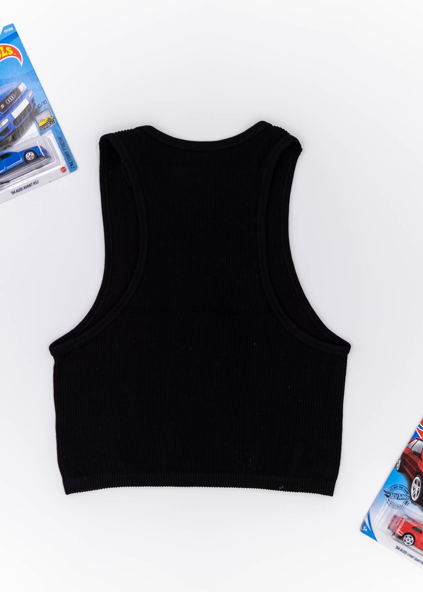 A black Audi crop top for women. Photo is a blank canvas back view of the top with an embroidered imola yellow Audi B5 RS4. Fabric composition is polyester, and elastine. The material is stretchy, ribbed, and non-transparent. The style of this shirt is sleeveless, with a crewneck neckline.