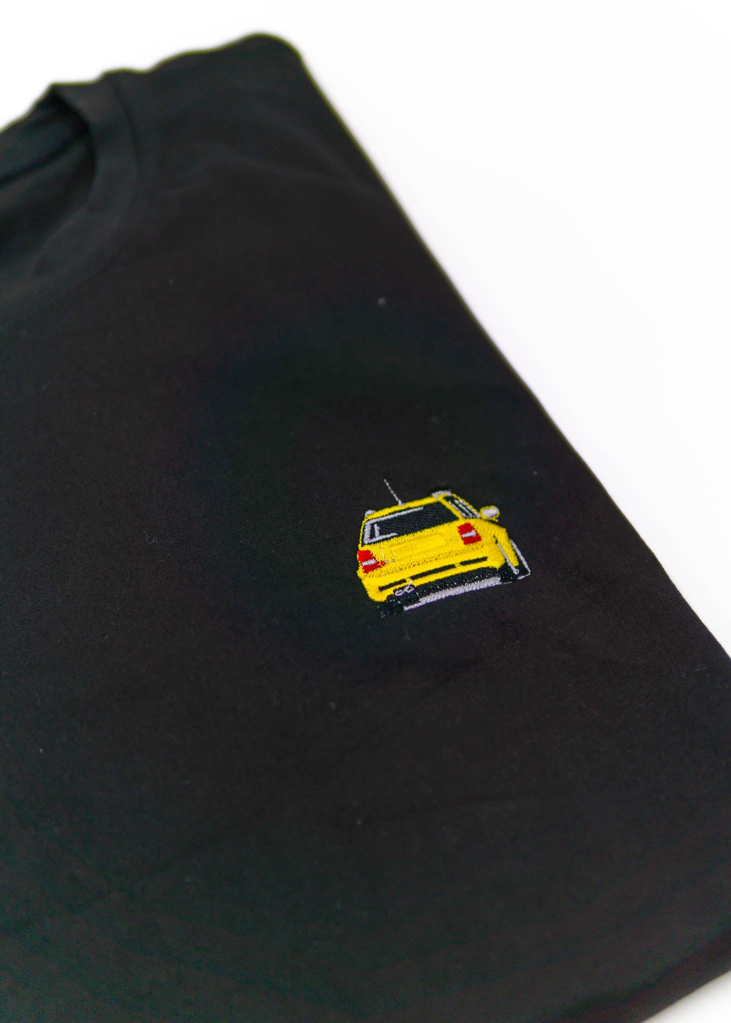A black Audi t-shirt for men. Photo is a close up view of the shirt with an embroidered Imola Yellow Audi B5 RS4. Fabric composition is polyester, and cotton. The material is very soft, stretchy, non-transparent. The style of this shirt is short sleeve, with a crewneck neckline.