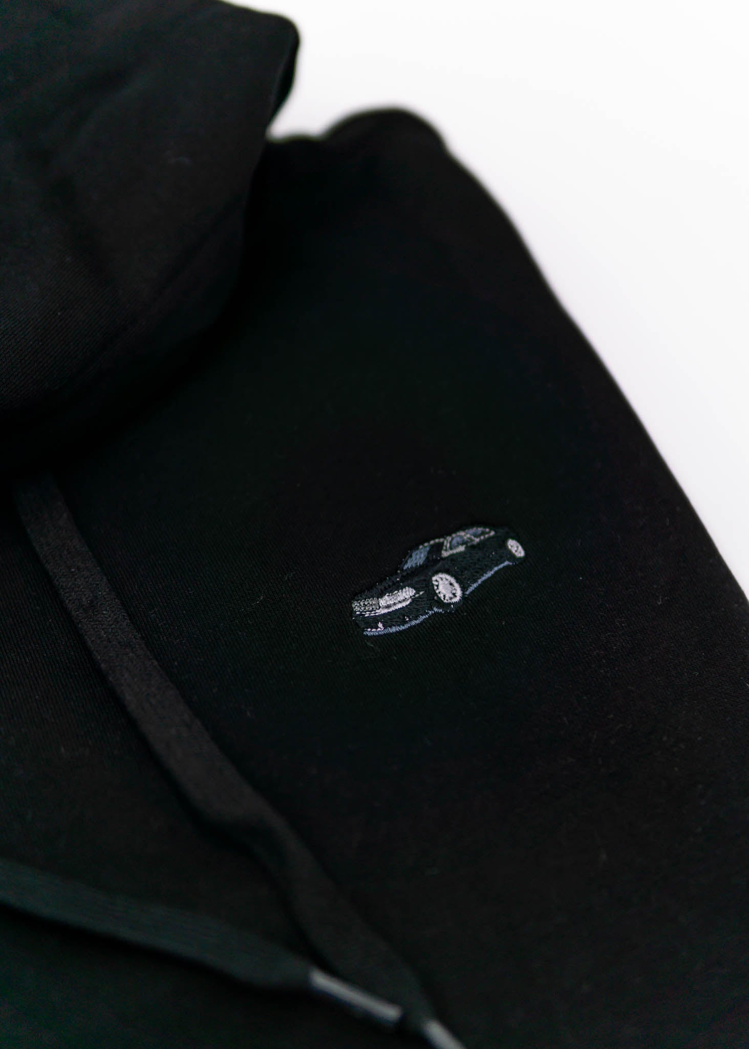 A black Audi hoodie for men and women. Photo is a close up view of the sweater with an embroidered Black Audi D2 S8. Fabric composition is cotton, polyester, and rayon. The material is very soft, stretchy, anti-shrink, and non-transparent. The style of this hoodie is long sleeve, crewneck with a hood, hooded, with embroidery on the left chest.