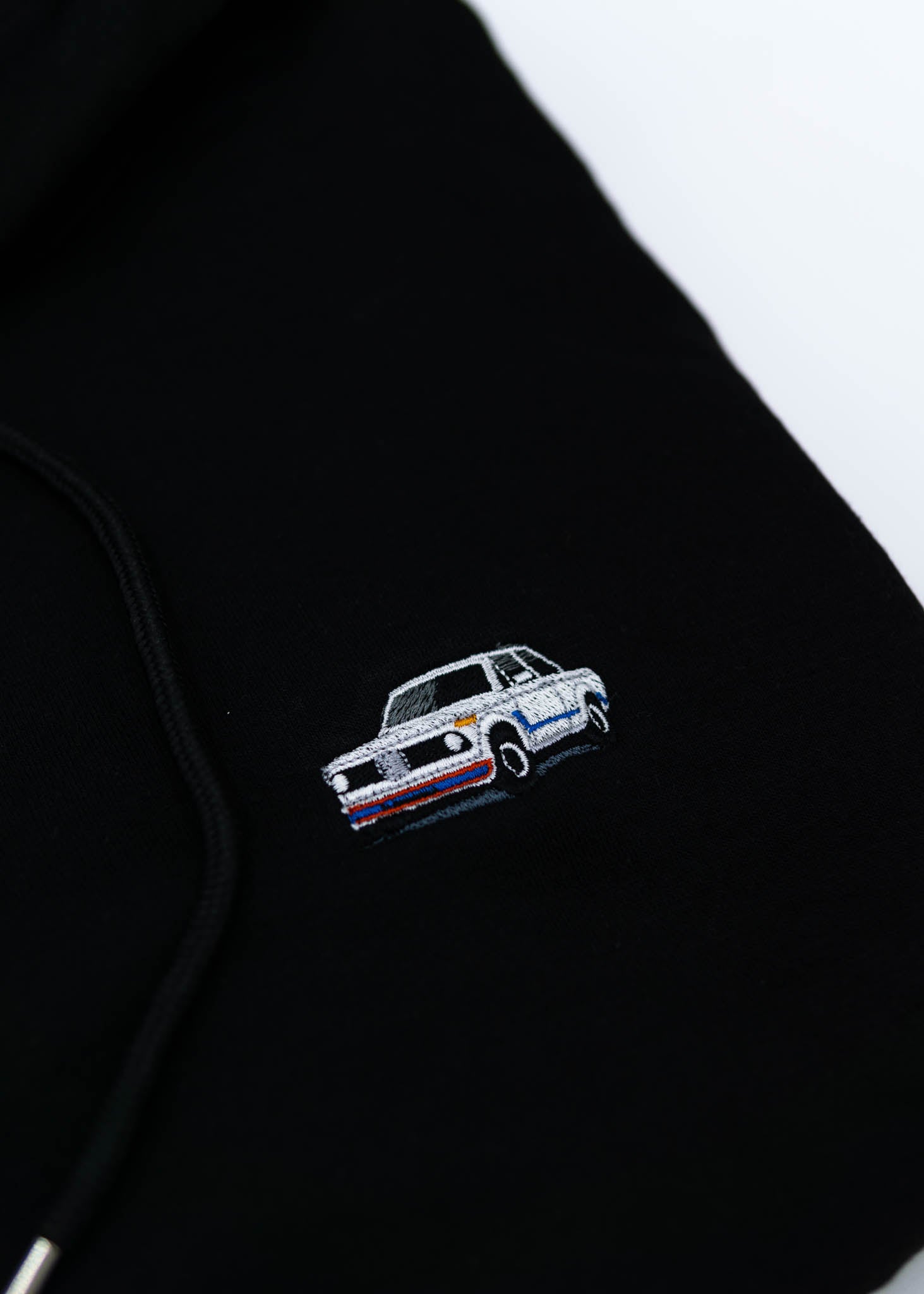 A black BMW cropped hoodie for women. Photo is a close up view of the cropped sweater with an embroidered BMW 2002 Turbo. Fabric composition is 100% cotton. The material is soft, comfortable, breathable, and non-transparent. The style of this crop hoodie is long sleeve, crewneck with a hood, hooded, with embroidery on the chest.