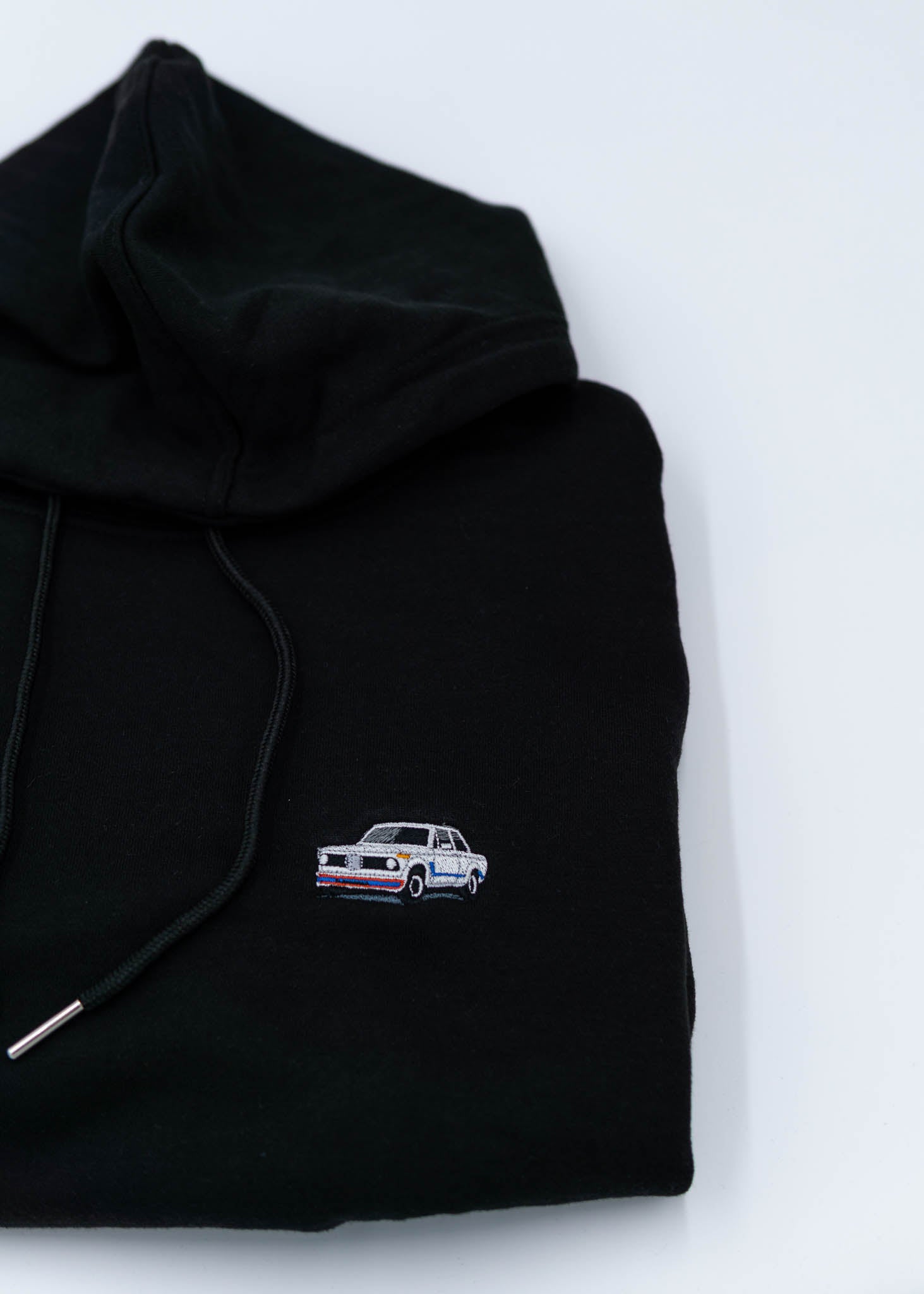 A black BMW cropped hoodie for women. Photo is a close up view of the cropped sweater with an embroidered BMW 2002 Turbo. Fabric composition is 100% cotton. The material is soft, comfortable, breathable, and non-transparent. The style of this crop hoodie is long sleeve, crewneck with a hood, hooded, with embroidery on the chest.