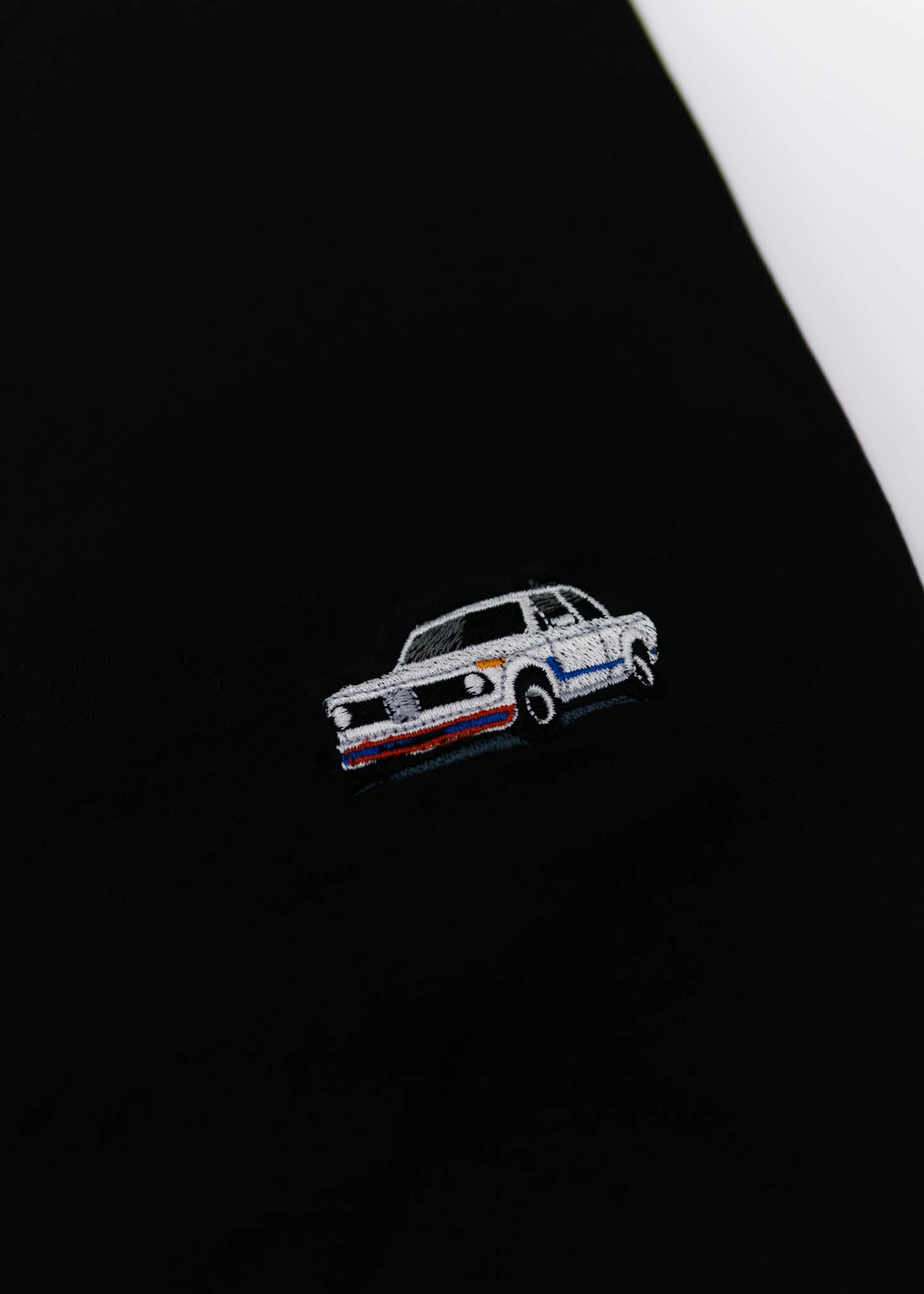 A black BMW 2002 Turbo t-shirt for men. Photo is a close up view of the shirt with an embroidered 2002 Turbo. Fabric composition is a polyester and cotton mix. The material is very soft, stretchy, non-transparent. The style of this shirt is short sleeve, with a crewneck neckline.