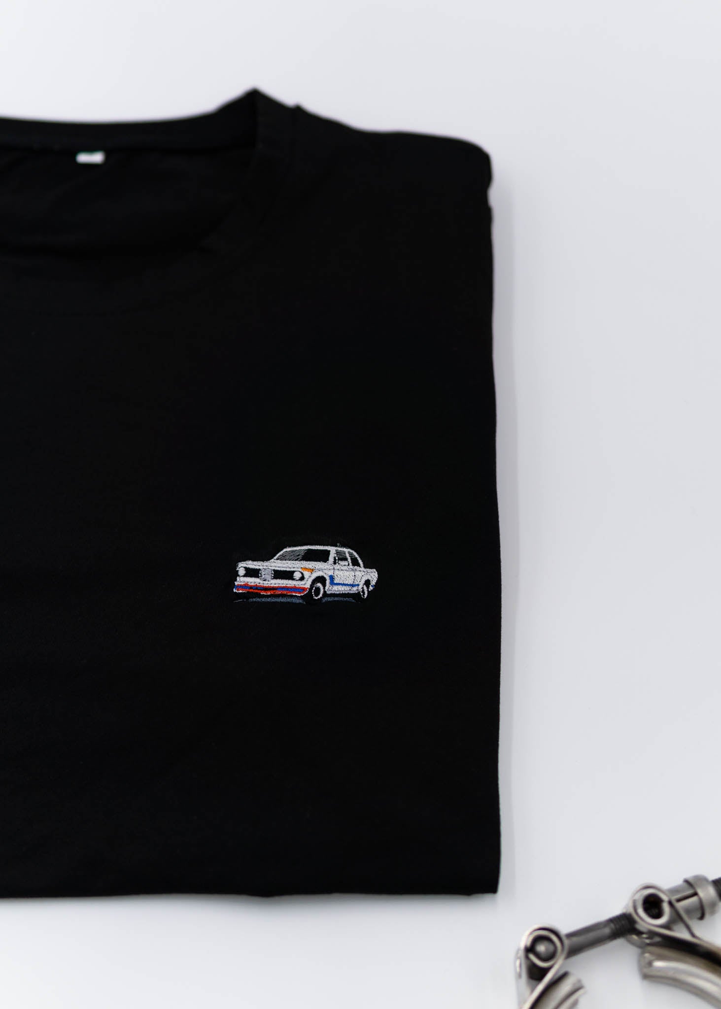 A black BMW 2002 Turbo t-shirt for men. Photo is a close up view of the shirt with an embroidered 2002 Turbo. Fabric composition is a polyester and cotton mix. The material is very soft, stretchy, non-transparent. The style of this shirt is short sleeve, with a crewneck neckline.