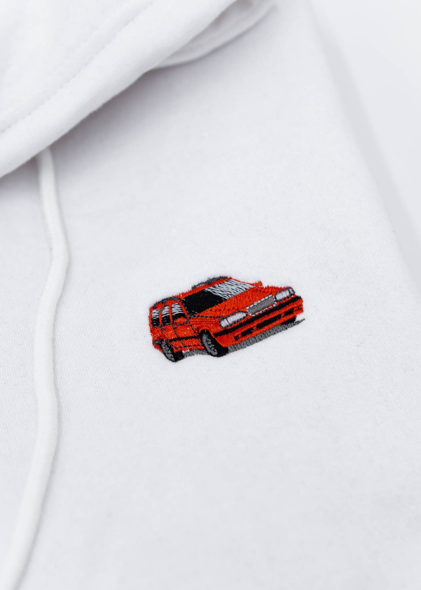 A white Volvo cropped hoodie for women. Photo is a close up view of the cropped sweater with an embroidered 850R. Fabric composition is 100% cotton. The material is soft, comfortable, breathable, and non-transparent. The style of this crop hoodie is long sleeve, crewneck with a hood, hooded, with embroidery on the chest.