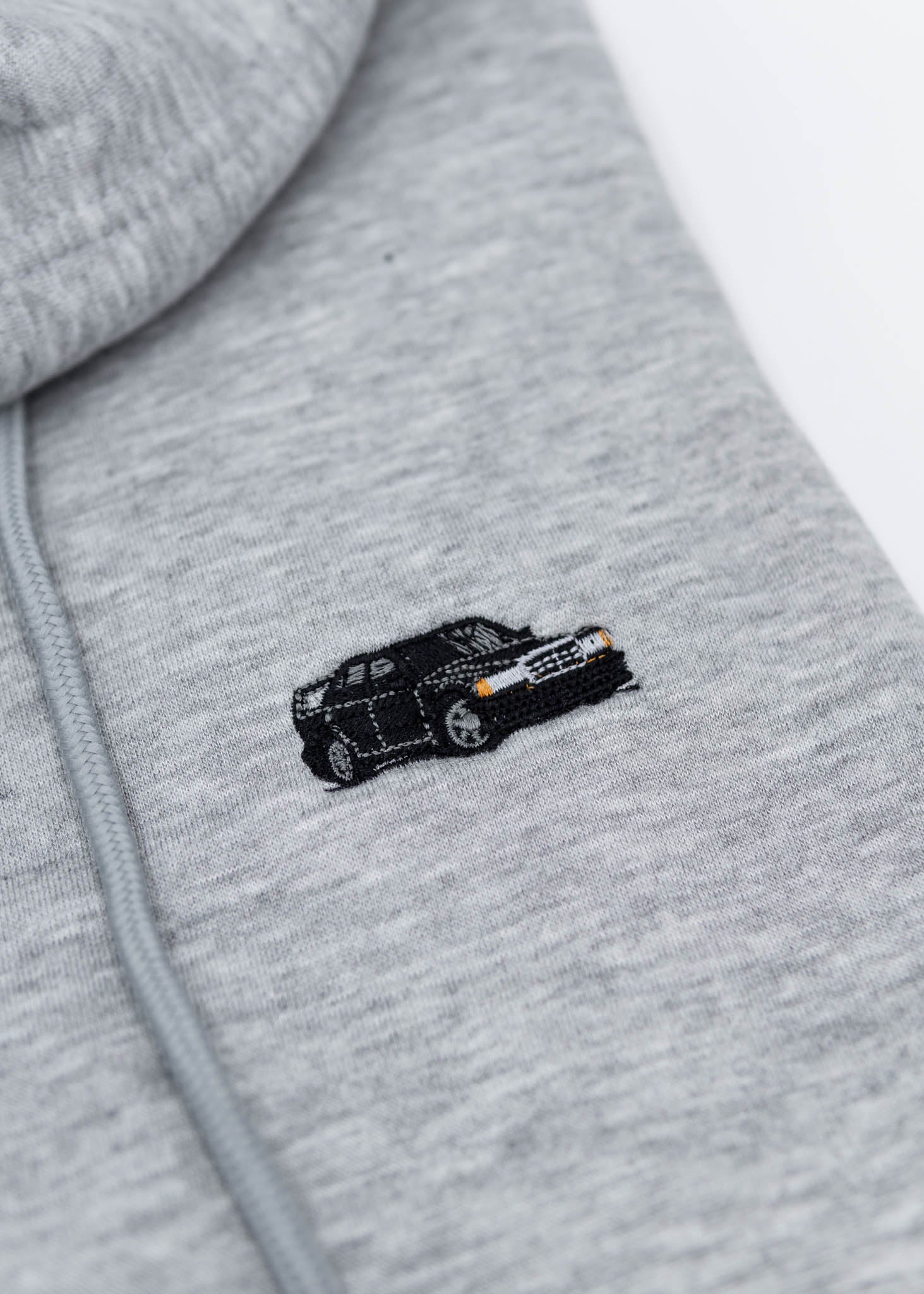 A grey Mercedes-Benz cropped hoodie for women. Photo is a close up view of the cropped sweater with an embroidered W201 190E 2.5-16 Evo II. Fabric composition is 100% cotton. The material is soft, comfortable, breathable, and non-transparent. The style of this crop hoodie is long sleeve, crewneck with a hood, hooded, with embroidery on the chest.