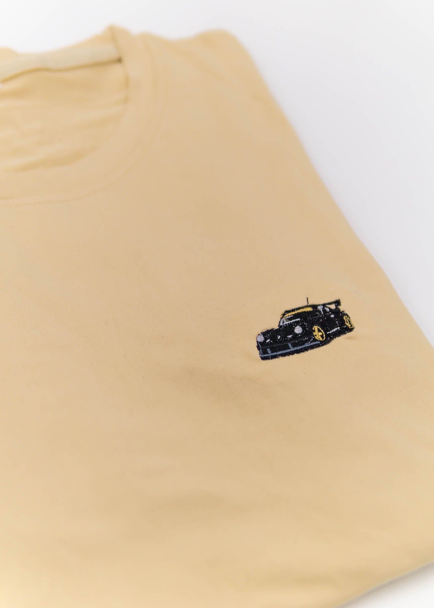 A Khaki RWB Porsche 930 911 Turbo T-Shirt for men. Photo is a close up view of the shirt with Akira Nakai's RWB Porsche 930 911 Turbo Stella Artois. Fabric composition is a polyester, and cotton mix. The material is very stretchy, soft, comfortable, and non-transparent. The style of this shirt is short sleeve, with a crewneck neckline.