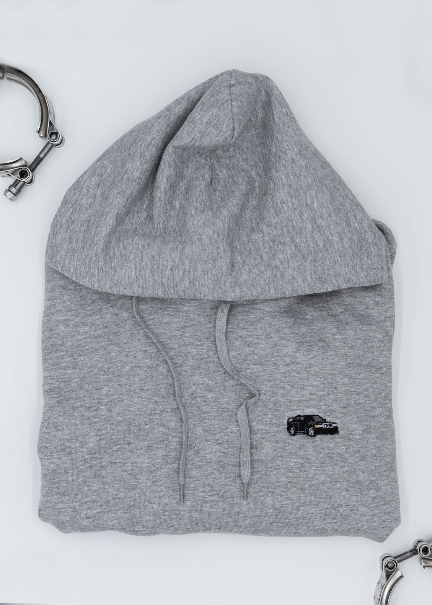 A grey Mercedes-Benz unisex hoodie for men and women. Photo is a close up view of the sweater with an embroidered Mercedes-Benz W201 190E 2.5-16 Evo II. Fabric composition is cotton, polyester, and rayon. The material is very soft, stretchy, and non-transparent. The style of this hoodie is long sleeve, crewneck with a hood, hooded, with embroidery on the left chest.