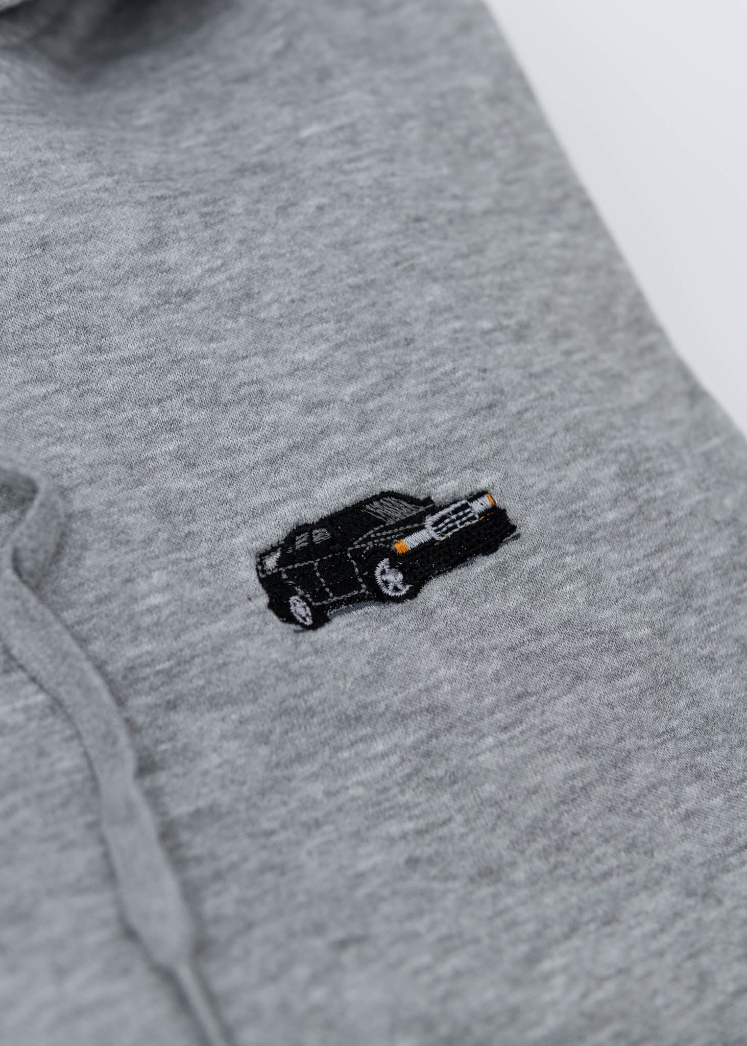 A grey Mercedes-Benz unisex hoodie for men and women. Photo is a close up view of the sweater with an embroidered Mercedes-Benz W201 190E 2.5-16 Evo II. Fabric composition is cotton, polyester, and rayon. The material is very soft, stretchy, and non-transparent. The style of this hoodie is long sleeve, crewneck with a hood, hooded, with embroidery on the left chest.