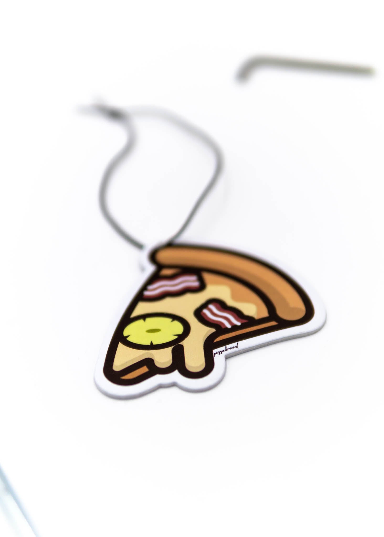 A pizzabrand pineapple and bacon pizza air freshener. Photo is a close up of the car air freshener with string.