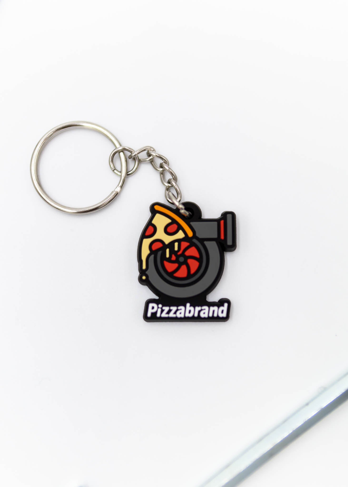 A pizzabrand pizza and turbo keychain. Made of rubber and stainless steel. Photo is of a close up of the pizza melting on a turbo with the brand name.