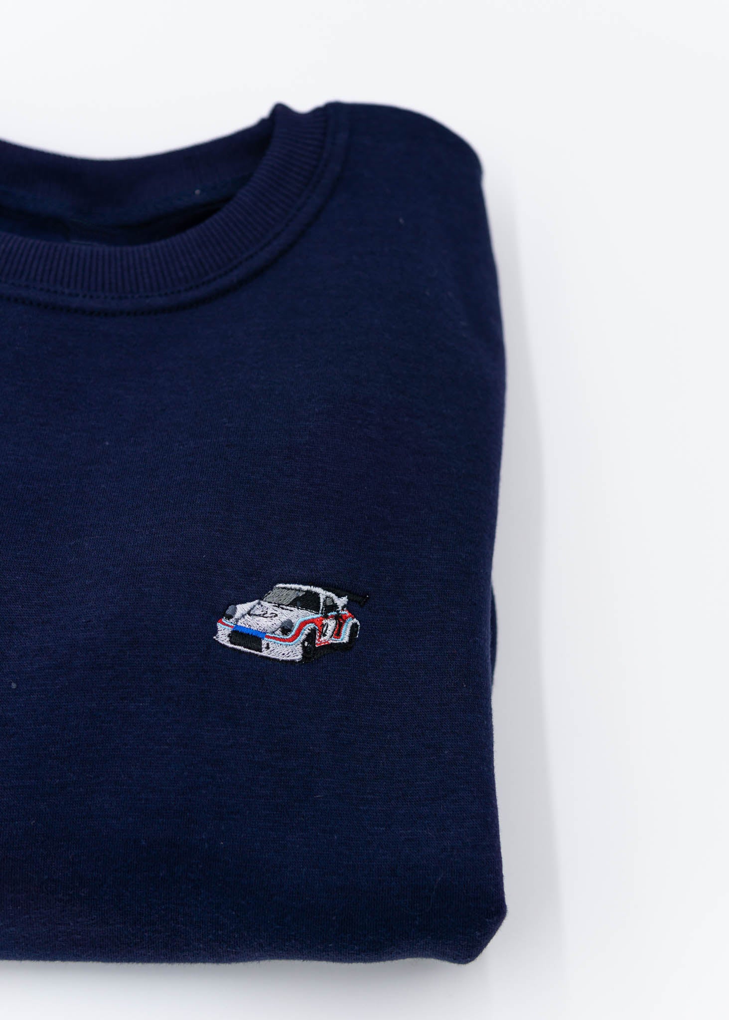 A navy blue Porsche race car crewneck sweater for men. Photo is a close up of the sweater with an embroidered Martini R13 Porsche 911 Carrera RSR 2.1 Turbo . Fabric is 100% cotton and high quality and fits to size. The style is long sleeve, crew neck, and embroidery on left chest.