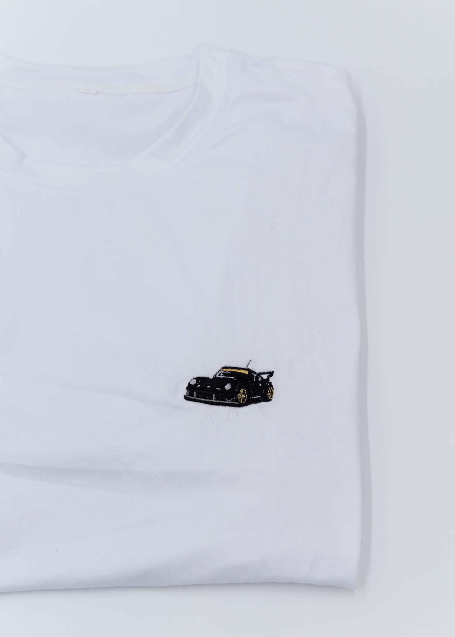 A white Porsche T-Shirt for men. Photo is a close up of the shirt with an embroidered RWB Porsche 930 911 Turbo Stella Artois. Fabric composition is 100% polyester. The material is very stretchy, soft, comfortable, breathable, and non-transparent. The style of this shirt is short sleeve, with a crewneck neckline.