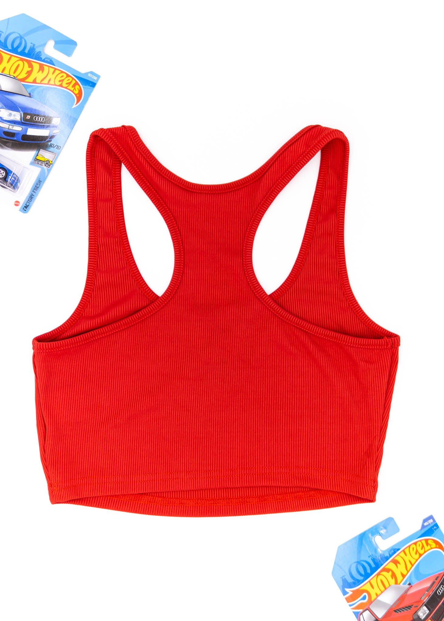 A red Audi crop top for women. Photo is a back view of the top with an embroidered Audi Sport Quattro S1 E2. Fabric composition is polyester, and cotton. The material is stretchy, ribbed, and non-transparent. The style of this shirt is sleeveless, with a scoop neckline.