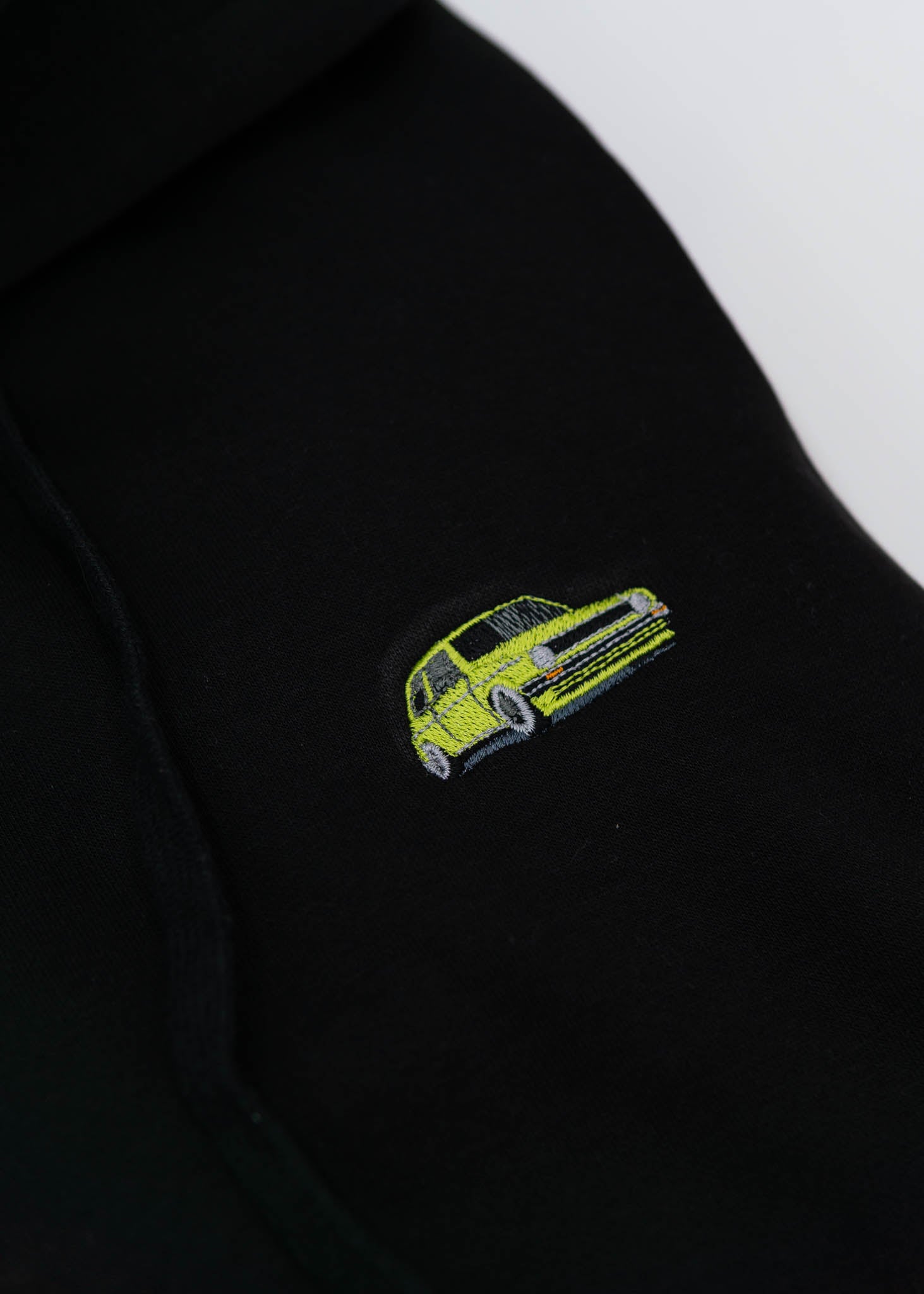 A black VW Volkswagen unisex hoodie for men and women. Photo is a close up of the sweater with an embroidered modified green Mk1 Golf. Fabric composition is cotton, polyester, and rayon. The material is very soft, stretchy, and non-transparent. The style of this hoodie is long sleeve, crewneck with a hood, hooded, with embroidery on the left chest.