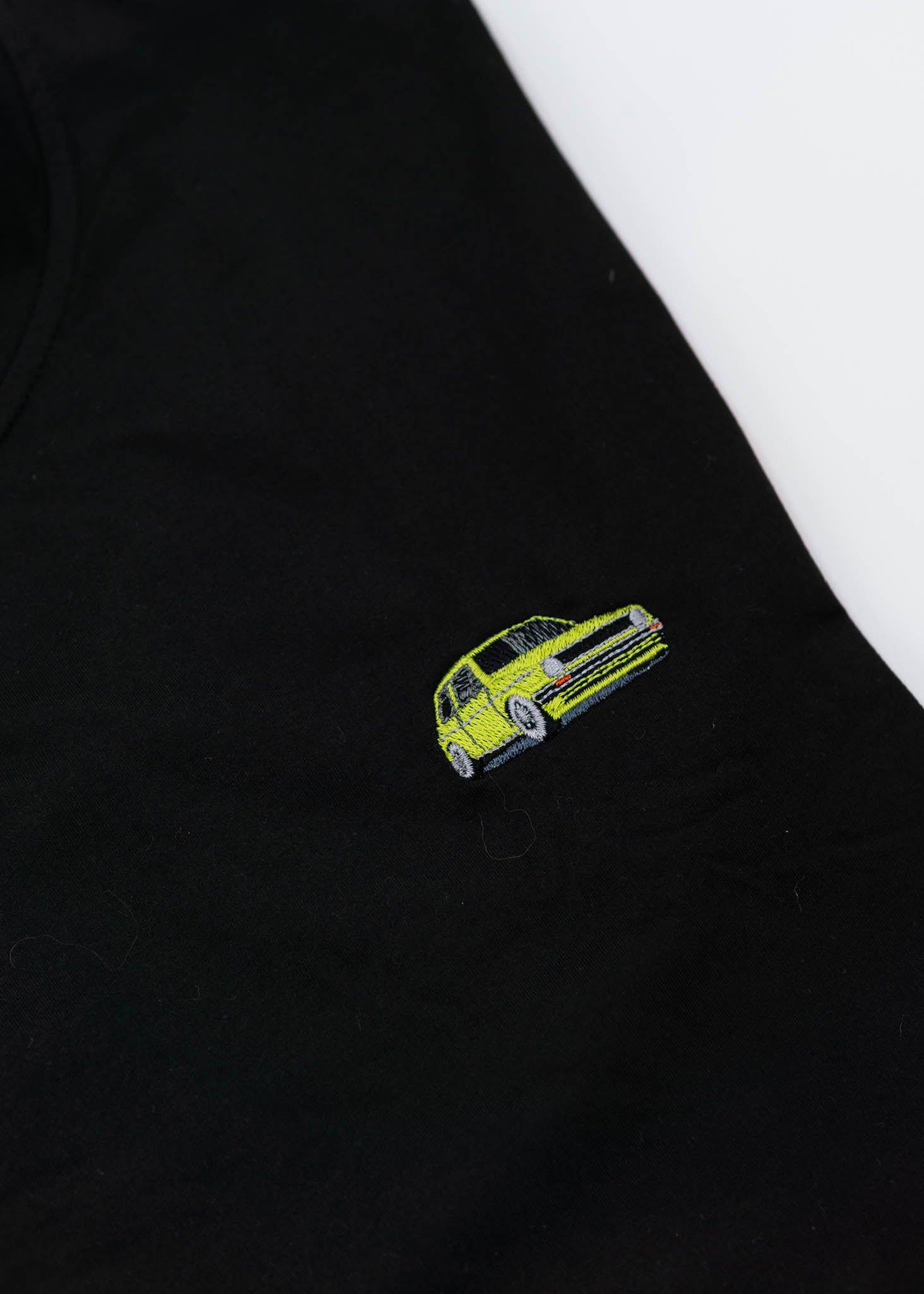 A black VW VolkswagenT-Shirt for men. Photo is a close up of the shirt with an embroidered modified green Mk1 Golf. Fabric composition is 100% polyester. The material is very stretchy, soft, comfortable, breathable, and non-transparent. The style of this shirt is short sleeve, with a crewneck neckline.
